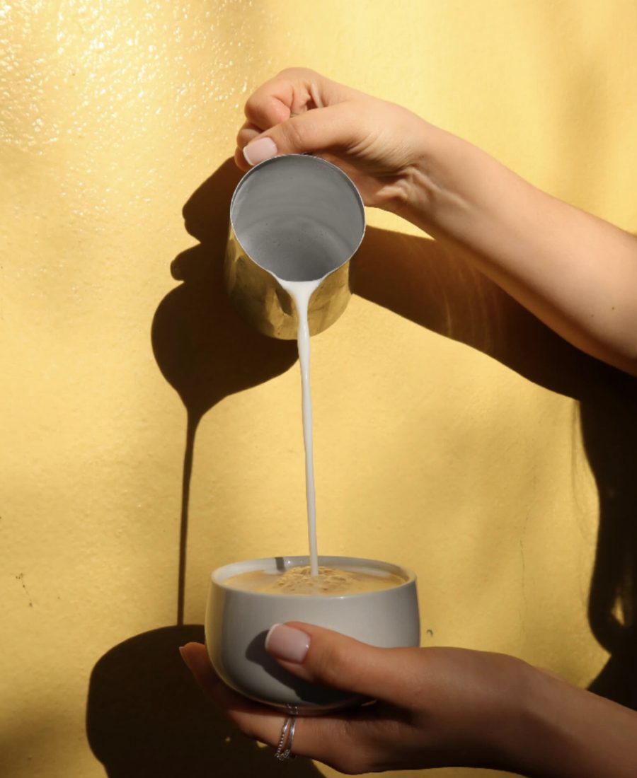 Milchschaum wird in eine Cappuccino-Tasse gegossen, Sonnenlicht auf gelber Wand